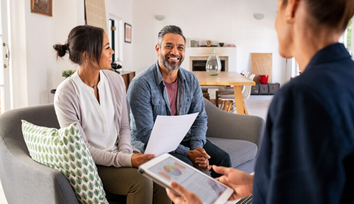 Happy mature couple discussing investments with financial broker during meeting at home. Happy middle eastern man and hispanic woman discussing about financial planning with consultant at home. Financial consultant presenting new investment plan to smiling mature couple at home.